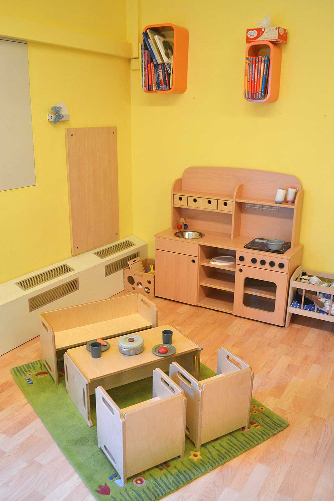 Raumecke mit einer kleinen Holzküche für Kinder und dazu passendem Tisch mit Stühlen.